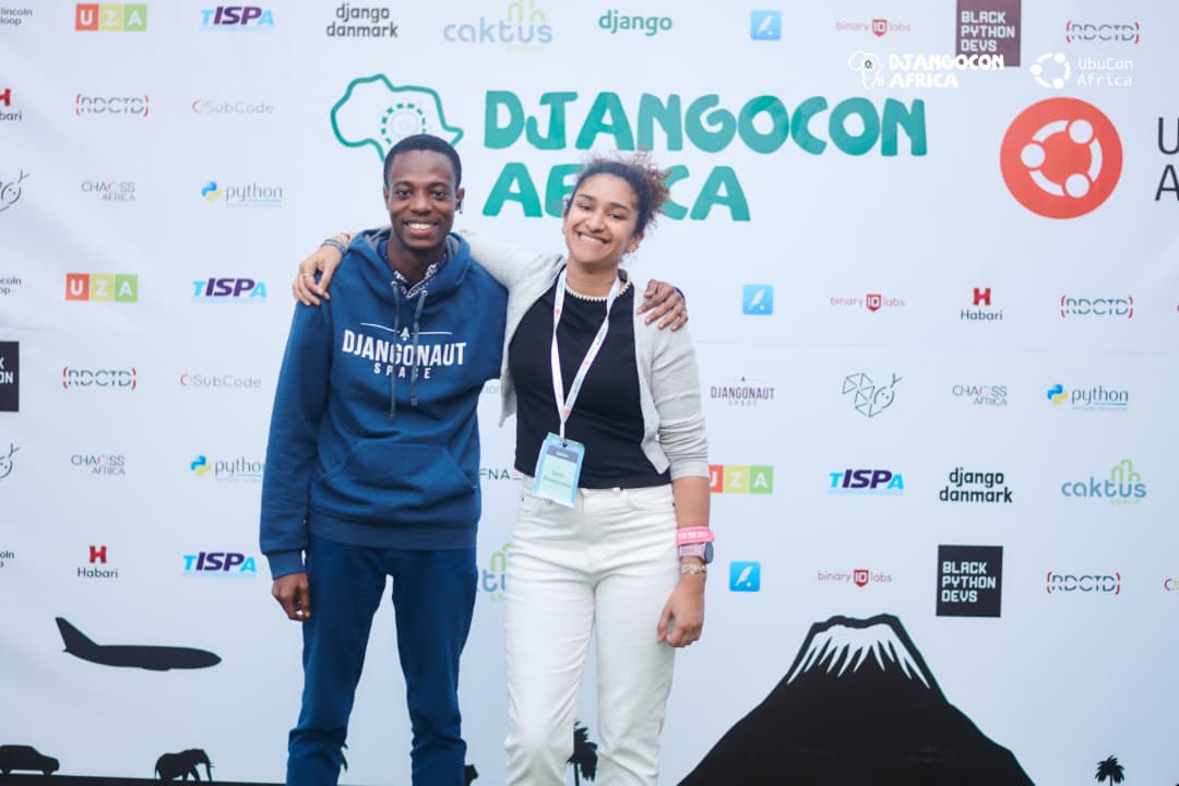 Philip at DjangoCon Africa sponsor wall wearing Djangonaut Space hoodie